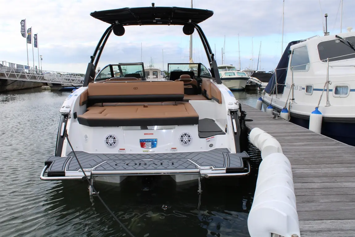 Cobalt boat moored at a marina, featuring a spacious tan interior and water access beside a wooden dock and other boats.